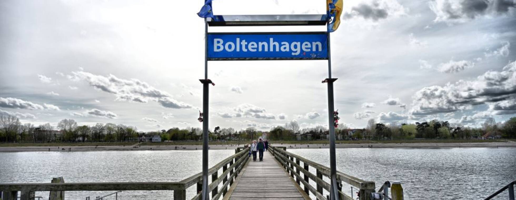 Blick über den Steg aufs Wasser mit dem Orstschild von Boltenhagen