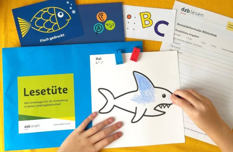 Zwei Kinderhände malen einen Hai aus. Daneben ist der Inhalt der Lesetüte ausgebreitet.