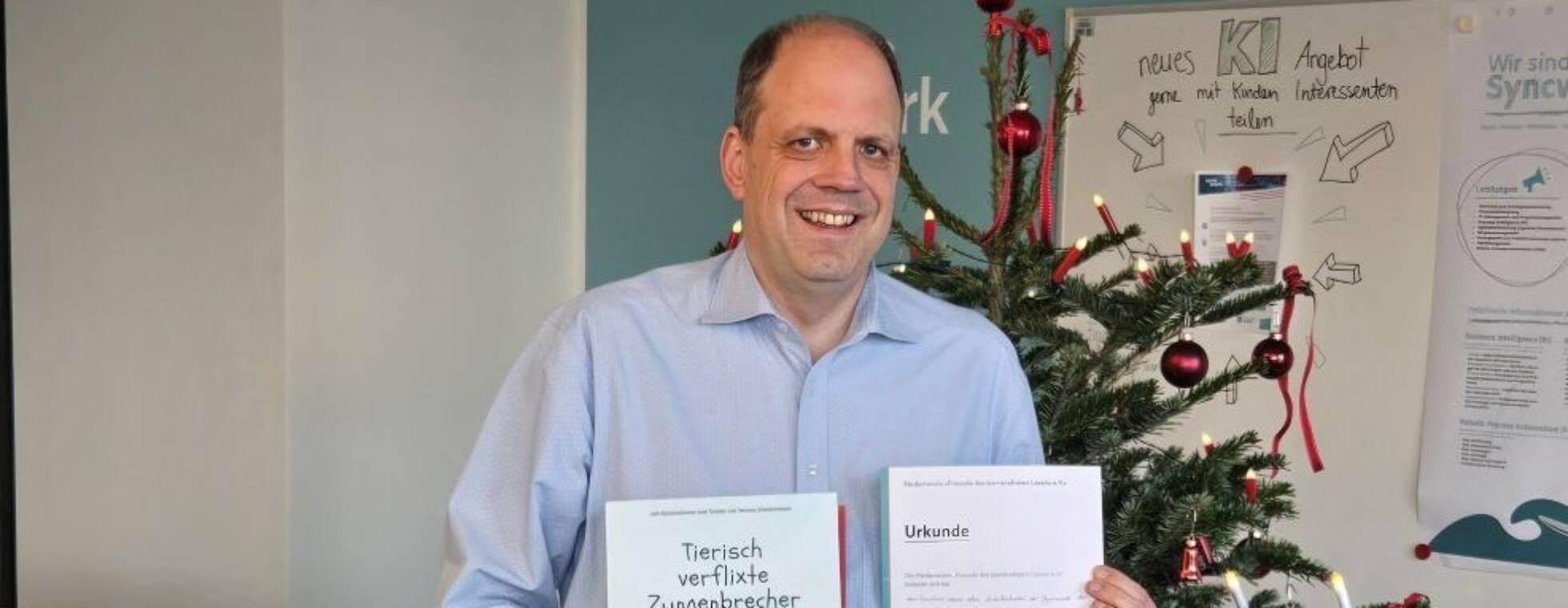Martin Hartmann, Vorstandsmitglied der Syncwork-AG mit dem Kinderbuch und einer Patenchaftsurkunde vor einem Weihnachtsbaum