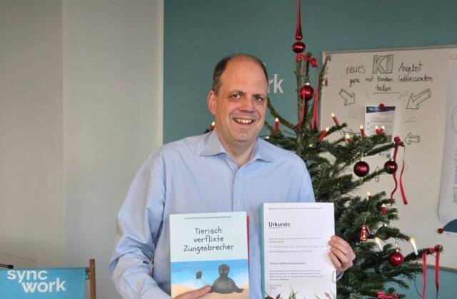 Martin Hartmann, Vorstandsmitglied der Syncwork-AG mit dem Kinderbuch und einer Patenchaftsurkunde vor einem Weihnachtsbaum