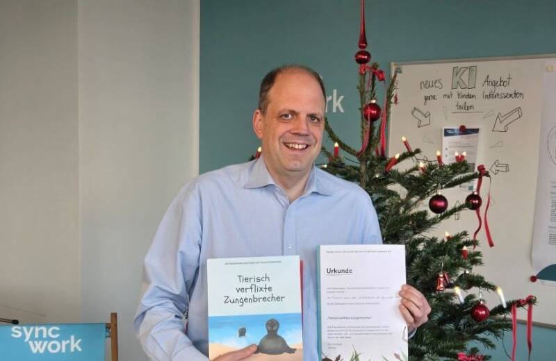 Martin Hartmann, Vorstandsmitglied der Syncwork-AG mit dem Kinderbuch und einer Patenchaftsurkunde vor einem Weihnachtsbaum