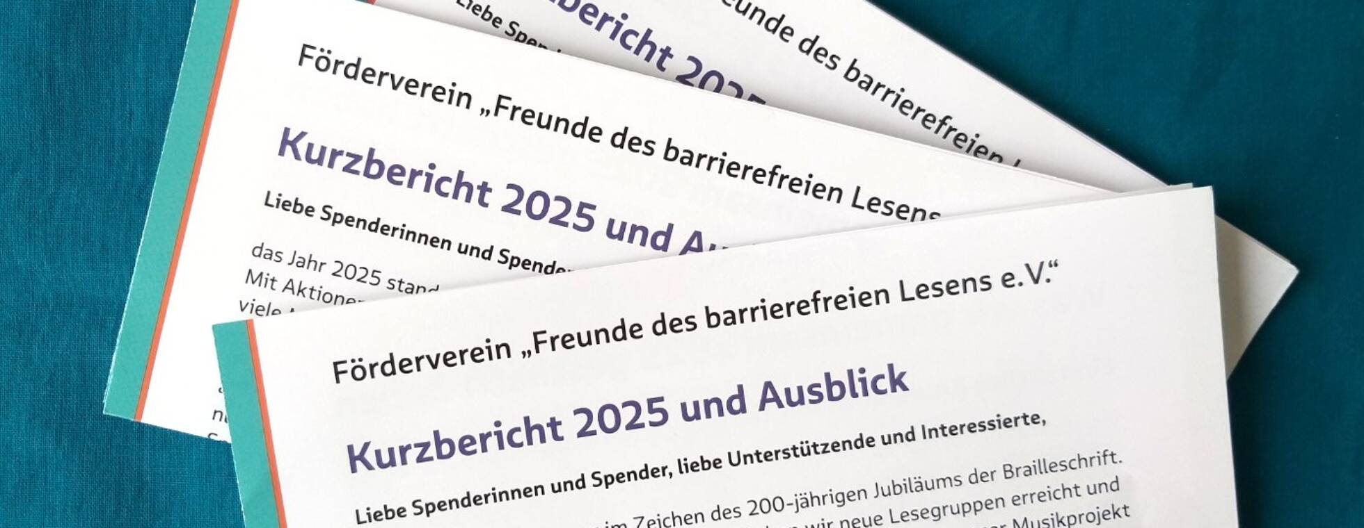 drei gefaltete Exemplare des Jahresberichts 2025 vor türkisblauem Hintergrund